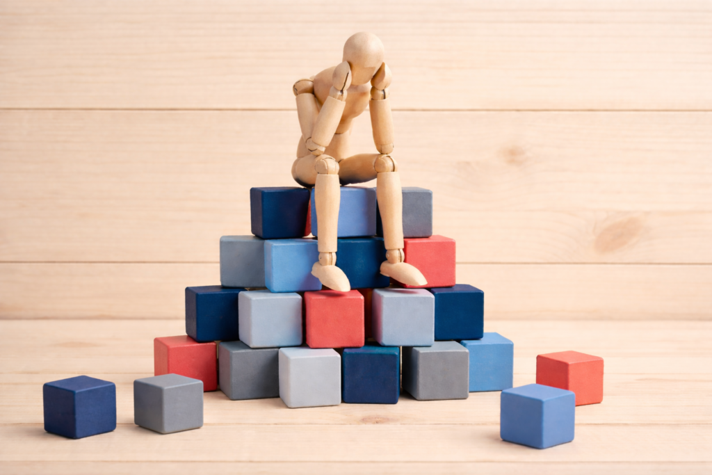 Emotional blocks concept image showing figure sitting on coloured blocks representing anxiety, imposter syndrome and low self-esteem support
